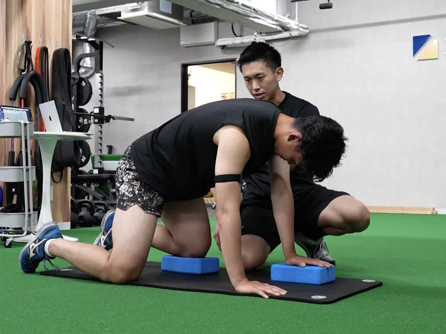 選手の動きに手を添えて個別に指導するトレーナー
